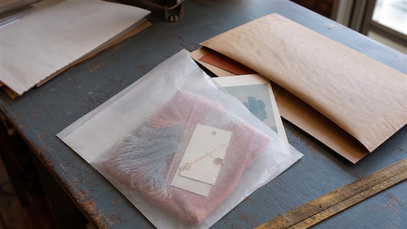 Glassine bag protecting a folded scarf, stationery and small retail products at an ecommerce packing bench