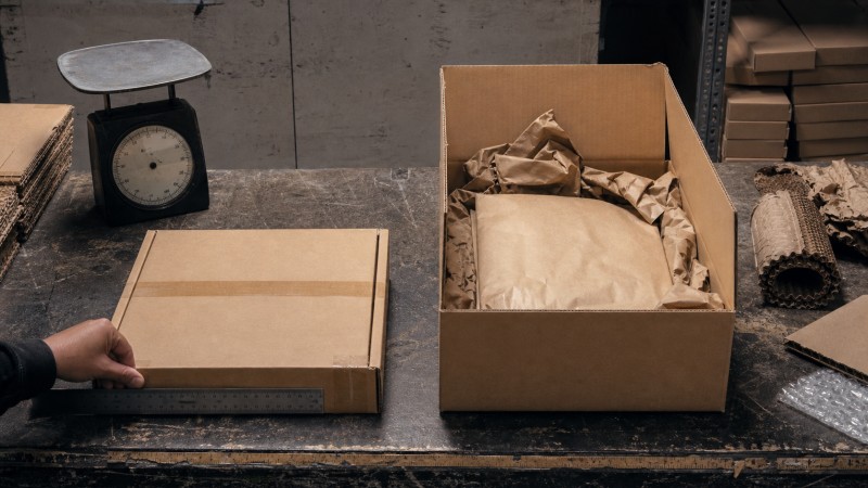 Right-sized laptop shipping box compared with an oversized carton and loose filler on an inspection table
