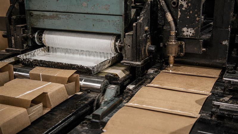 Water-based adhesive tray and hot-melt glue nozzle applying adhesive to paper cartons on a worn packaging production line