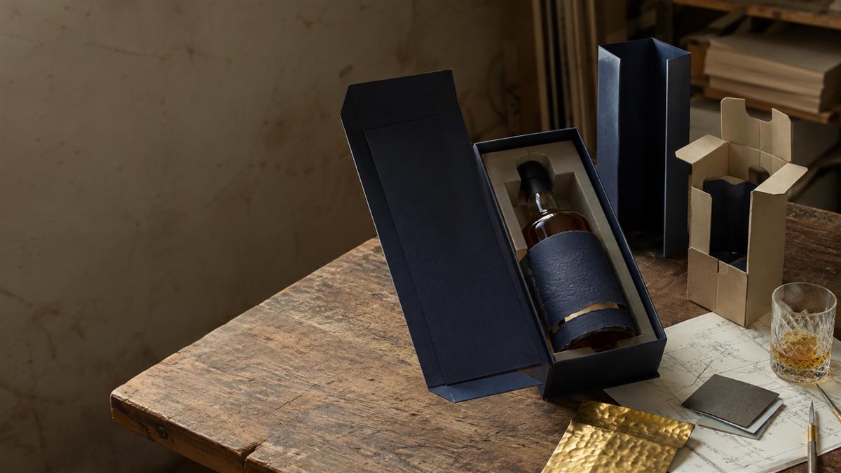 Premium whisky bottle in a dark rigid presentation box on a worn packaging workbench